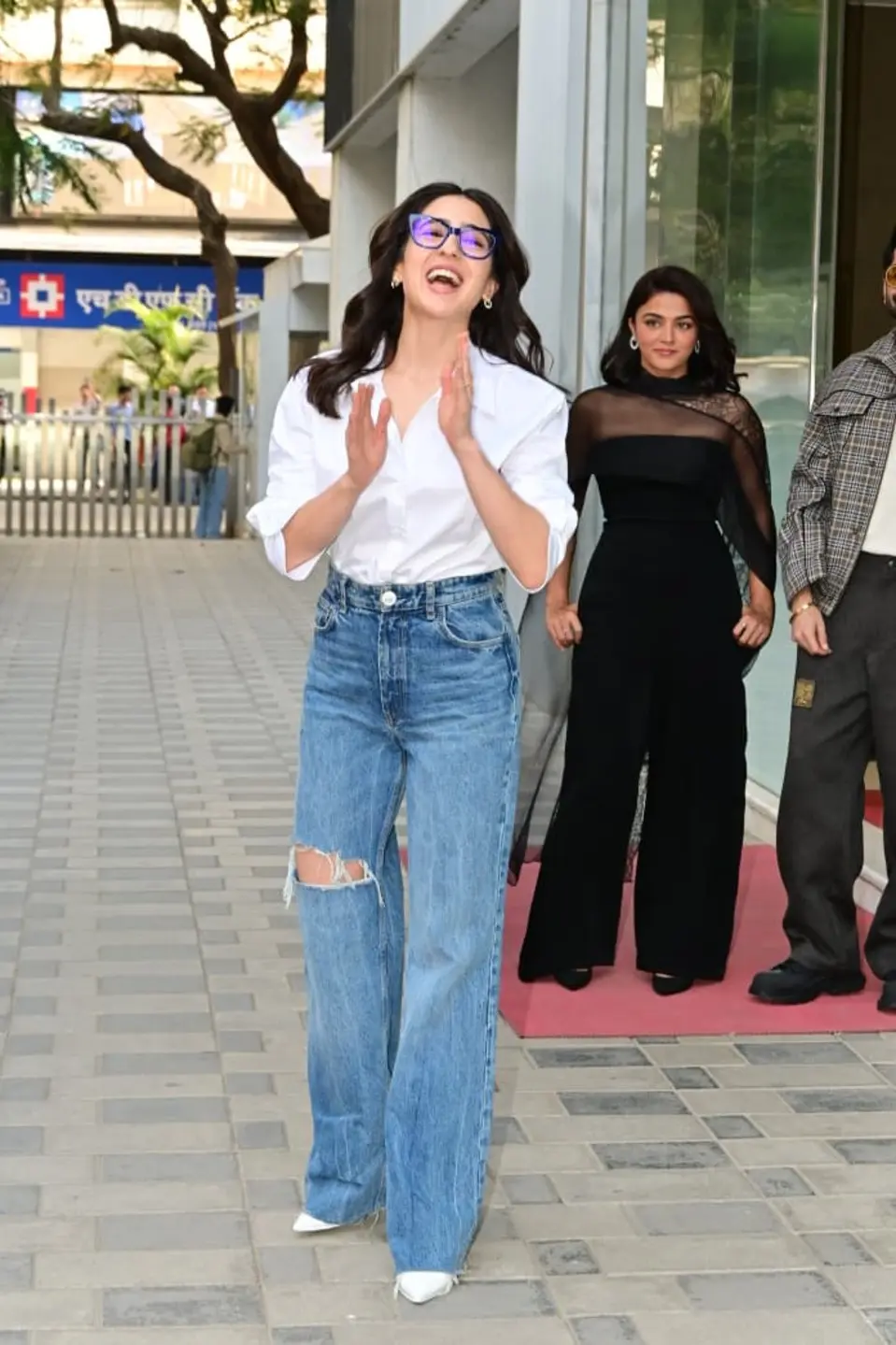 The outfit is elevated by her bold blue-rimmed glasses and pointed white heels.